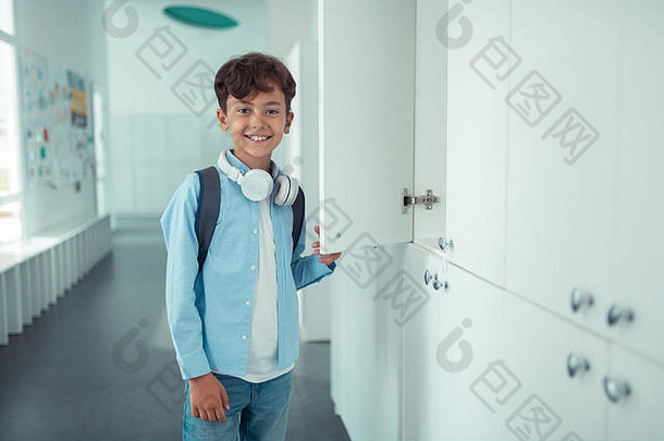 英俊的小学生穿耳机站学校储物柜