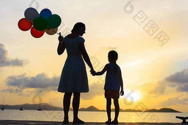 轮廓快乐妈妈。女儿群气球海海岸日落