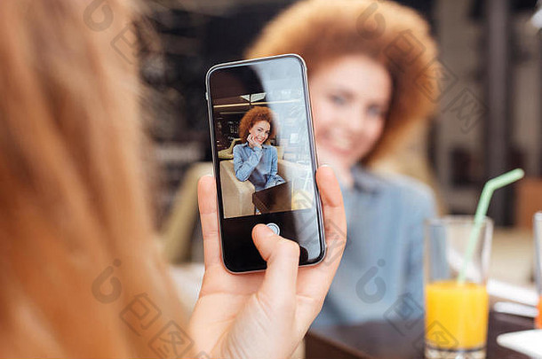 女持有智能手机采取图片快乐的美丽的红色头发的人年轻的女人坐着咖啡馆