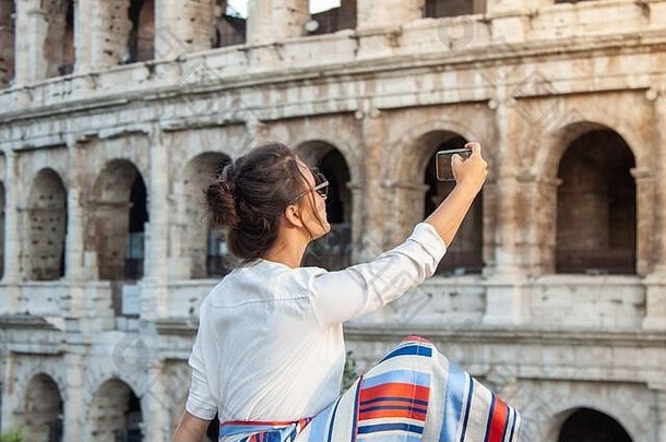 美丽的年轻的女人采取图片智能手机坐着前面罗马圆形大剧场罗马日落