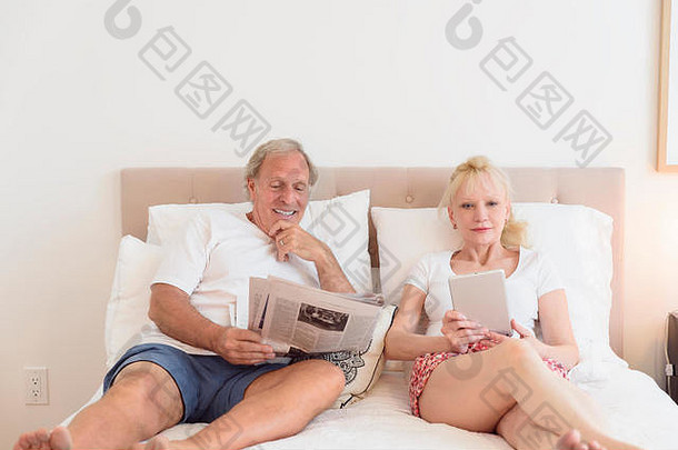 高加索人夫妇阅读报纸数字平板电脑床上