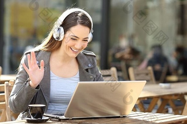 快乐女人穿无线耳机videocalling移动PC坐着咖啡馆阳台