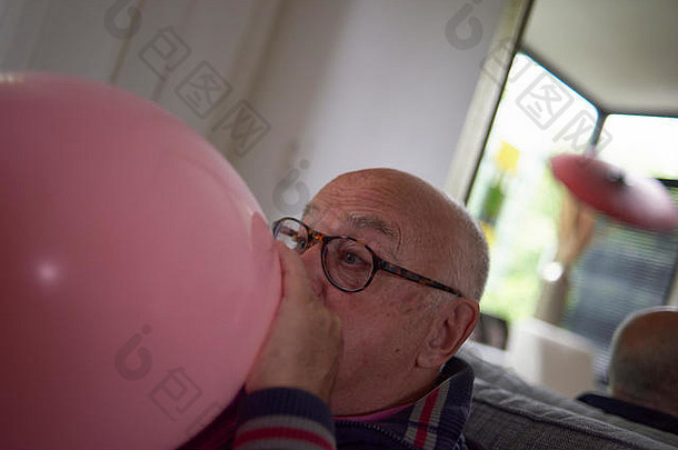 上了年纪的退休男人。吹大心形状的粉红色的气球装修房间生日聚会，派对