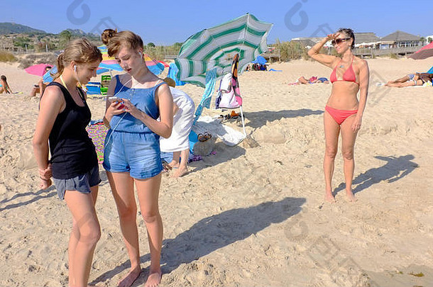 十几岁的女孩听电话海滩妈妈。背景