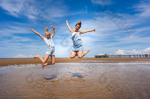 漂亮的女孩妈妈。穿粗布工作服跳高空气布莱克浦海滩著名的布莱克浦码头背景