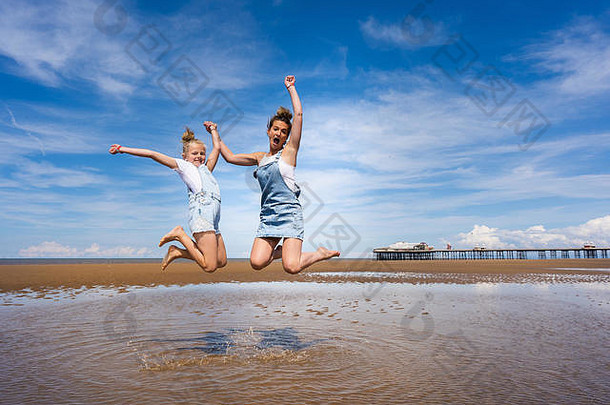 漂亮的女孩妈妈。穿粗布工作服跳高空气布莱克浦海滩著名的布莱克浦码头背景