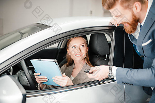 有胡子的推销员给车关键年轻的女人坐着车数字平板电脑