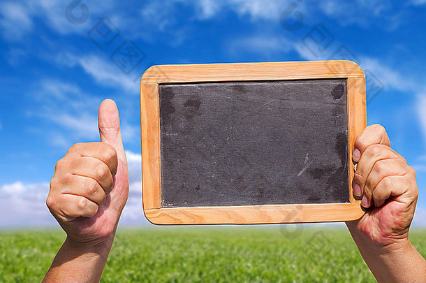 手持有空白板岩黑板上空气显示拇指背景绿色草地蓝色的天空