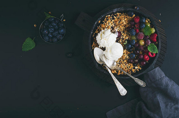 健康的早餐燕麦格兰诺拉麦片崩溃新鲜的浆果种子冰淇淋铁长柄平底煎锅锅黑暗木董事会黑色的背景