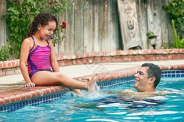 女孩穿泳装坐着在游泳池边溅父亲微笑
