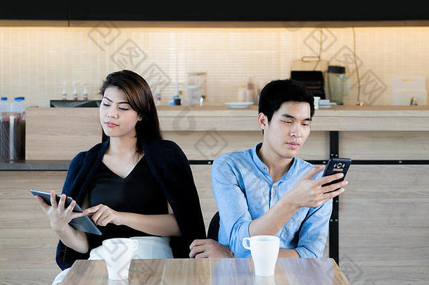 亚洲夫妇移动电话日期咖啡馆年轻的亚洲夫妇坐着智能手机忽略