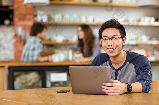 年轻的快乐的亚洲男人。眼镜移动PC坐着咖啡馆