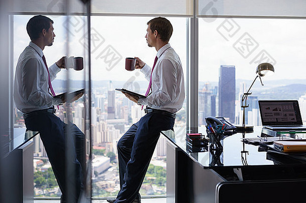 成人商人坐着桌子上现代办公室阅读新闻平板电脑杯咖啡男人。