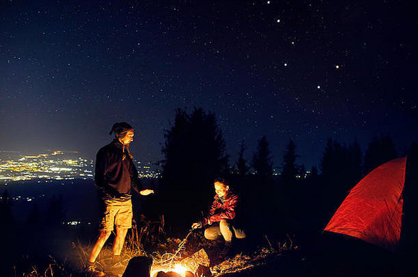快乐夫妇徒步旅行者温暖的手篝火晚上天空星星城市灯背景