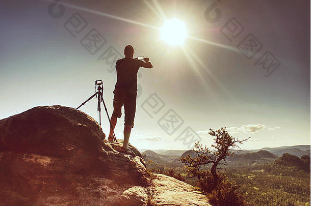 旅行者智能手机保持三脚架相机峰会摄影师采取照片日落山自然背景