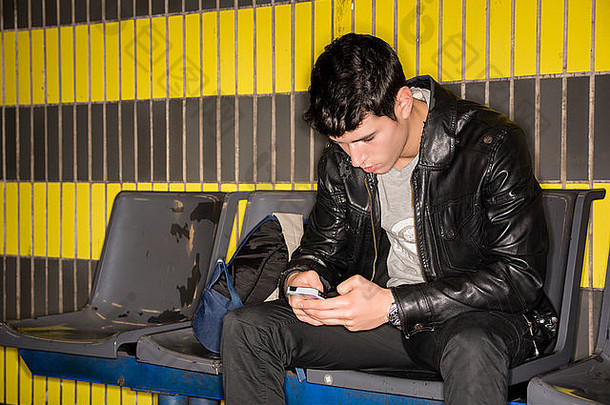 年轻的男人。坐着站打字智能手机等待地铁火车