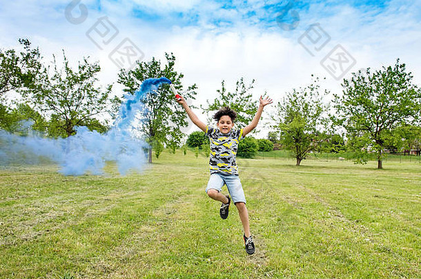 快乐无忧无虑的年轻的男孩玩蓝色的耀斑运行草落后于烟新鲜的绿色公园花园