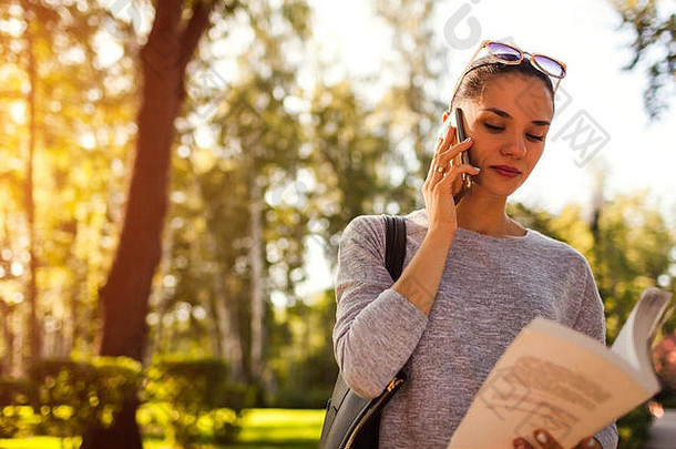 <strong>大学学生会</strong>说话的移动电话公园年轻的女人阅读书检查信息