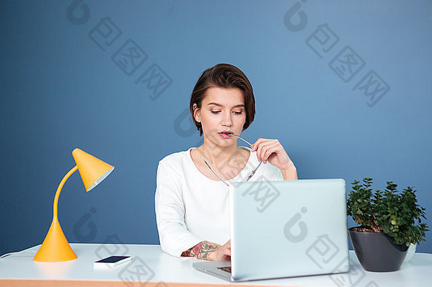 沉思的集中年轻的女人坐着表格工作移动PC蓝色的背景