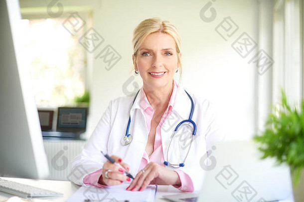 美丽的微笑女医生坐着前面电脑医生的办公室写作诊断