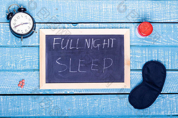 睡眠概念显示报警时钟睡觉药片眼睛面具黑色的董事会阅读完整的晚上睡眠饱经风霜的蓝色的背景