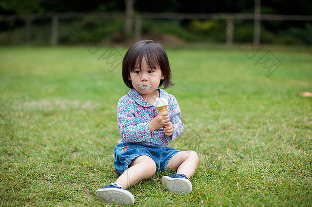 婴儿女孩坐着夏天草地吃冰淇淋