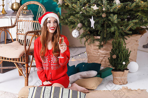 有吸引力的圣诞节女人穿圣诞老人他红色的毛衣坐着地板上舒适的一年云杉喝香槟一年圣诞节假期记忆礼物购物折扣商店雪少女圣诞老人老人化妆发型狂欢节