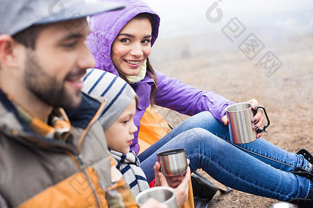 一边视图微笑家庭喝热茶金属杯坐着在户外