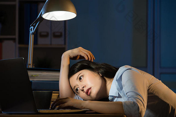 亚洲业务女人坐着桌子上困了工作加班晚些时候晚上在室内办公室背景