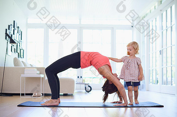 中期成人妈妈。练习瑜伽好奇的蹒跚学步的女儿