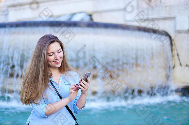 年轻的高加索人女孩聊天智能手机特莱维喷泉背景