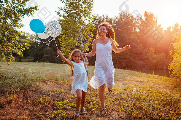 快乐女孩运行妈妈。持有baloons手家庭有趣的夏天公园日落国际儿童一天