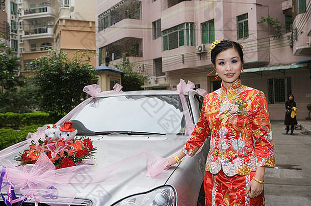 新娘穿着传统的中国人服装站装饰车微笑相机