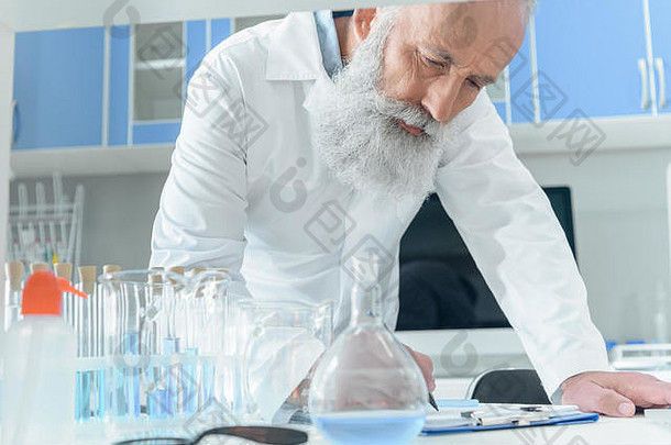 集中高级有胡子的科学家白色外套写作剪贴板坦勒烧瓶化学实验室