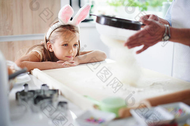 女孩看祖母筛选面粉复活节烘焙