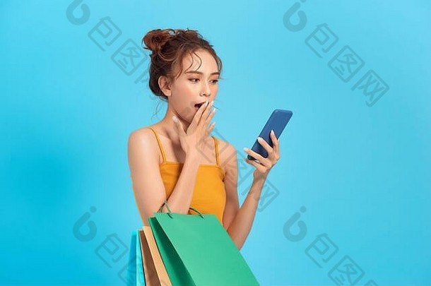 惊讶快乐女人持有便宜的纸购物袋电话屏幕读短信出售促销活动商店孤立的蓝色的使用