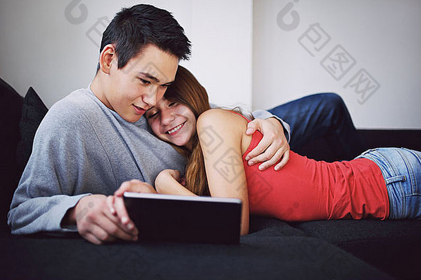 十几岁的夫妇爱说谎沙发平板电脑电脑年轻的亚洲夫妇看电影数字平板电脑