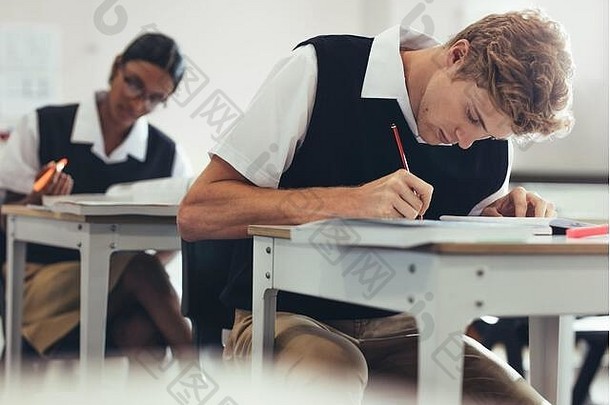 十几岁的男孩采取测试坐着桌子上教室高学校学生集中写作考试