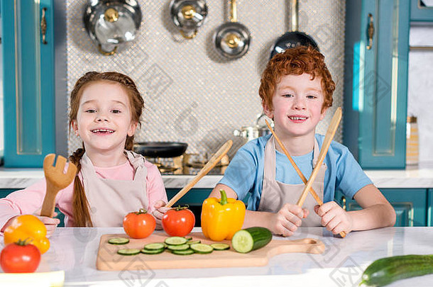 可爱的孩子们持有木餐具微笑相机烹饪厨房