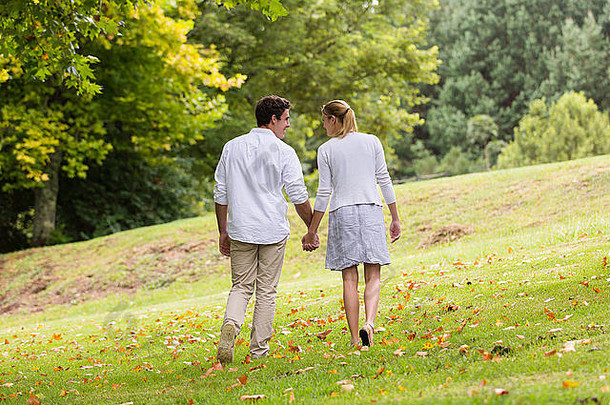 年轻夫妇手牵手在公园散步的后视图