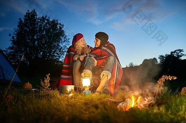 年轻的野营夫妇坐着篝火黄昏