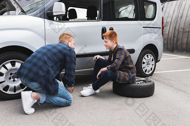 父亲提升车地板上杰克改变轮胎儿子