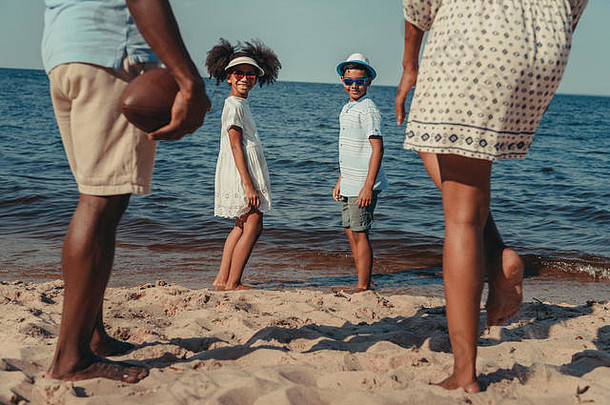 裁剪拍摄非洲美国家庭孩子们玩橄榄球球海滩
