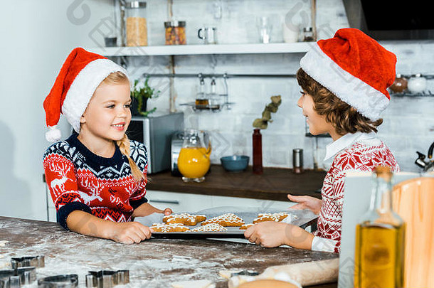 可爱的快乐孩子们圣诞老人帽子持有烘焙托盘姜饼干微笑