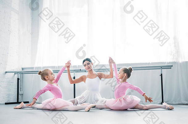 年轻的芭蕾舞老师孩子们图图裙子坐着持有手锻炼芭蕾舞学校