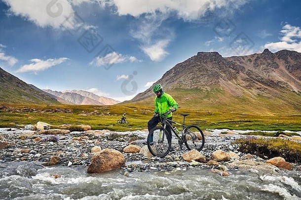 男人。山自行车穿越河野生山多云的天空背景