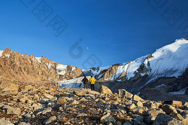 徒步旅行者黄色的黑暗夹克石头前面高雪山不断上升的月亮背景