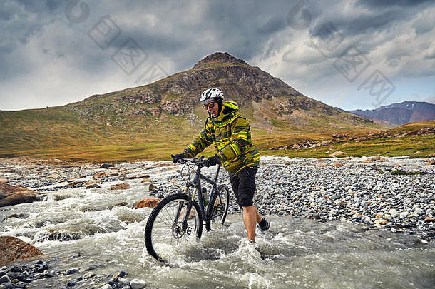 男人。山自行车穿越河野生山多云的天空背景