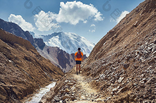 徒步旅行者橙色衬衫背包走小道雪峰会背景