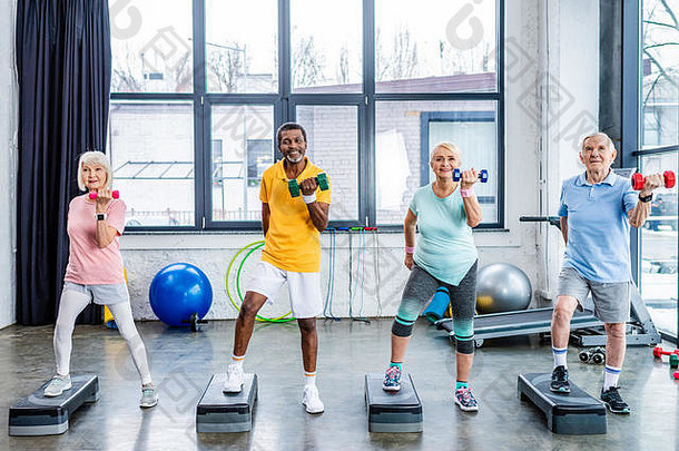 快乐高级多元文化的爱运动的人同步锻炼哑铃一步平台健身房